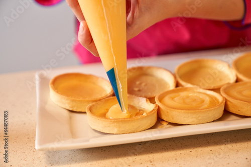 Crop female pastry chef making peaks of cream on tarts