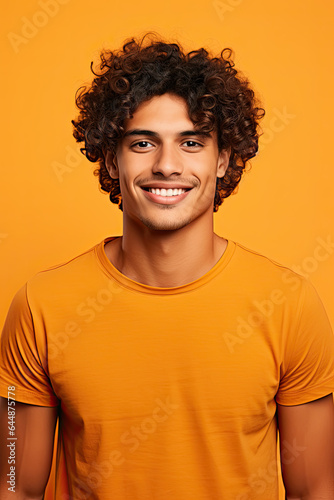 Portrait of a smiling young handsome male, with curly brown hair and an orange T-shirt, on an orange background