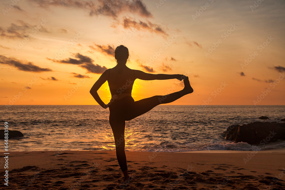 Silhouette of slim lady meditating on sea beach, workout doing yoga pose at sunset. Young woman performing sport exercises to restore strength and spirit. Healthy lifestyle concept. Copy ad text space