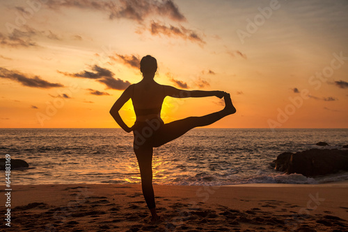 Silhouette of slim lady meditating on sea beach  workout doing yoga pose at sunset. Young woman performing sport exercises to restore strength and spirit. Healthy lifestyle concept. Copy ad text space