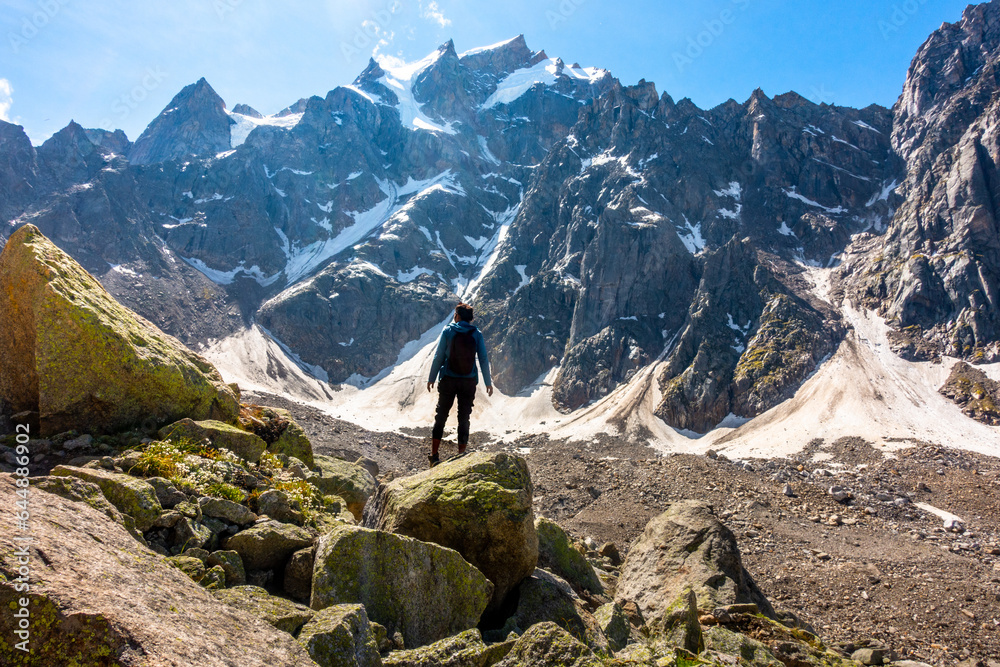 A person on a cliff facing Himalayan glacial peaks in Kinnaur Valley, Himachal Pradesh. Part of Hindu pilgrimage, Kinner Kailash Yatra.