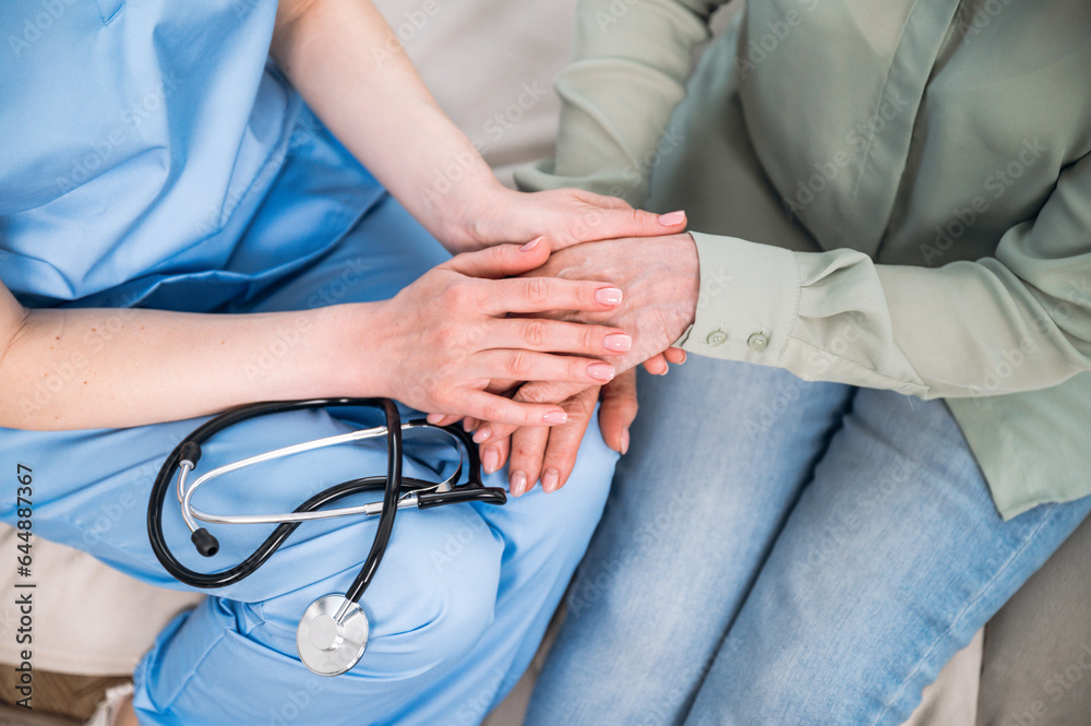 Fototapeta premium Woman doctor holding patient hands, caring elderly female at medical appointment