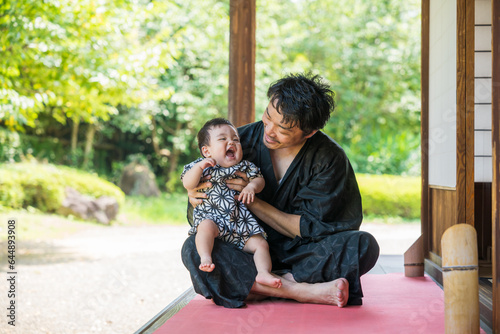 夏の緑が多い日本家屋の縁側で浴衣姿のパパに抱っこされて笑顔になる甚平姿の生後9か月の赤ちゃん