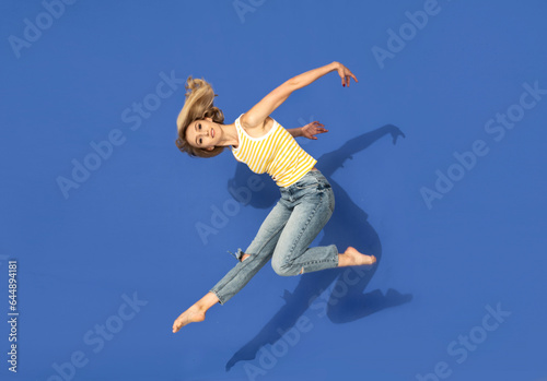 Young smiling woman dancing and jumping over blue studio background. Cute happy girl wearing fashionable jeans and top.