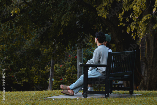 Asian couple sitting on a park bench relaxing, enjoying the gardens