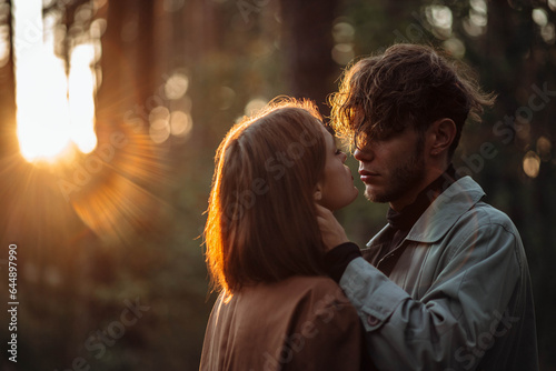 beautiful fashionable couple in love in the forest at sunset in autumn, romantic date in raincoats, trendy man and woman