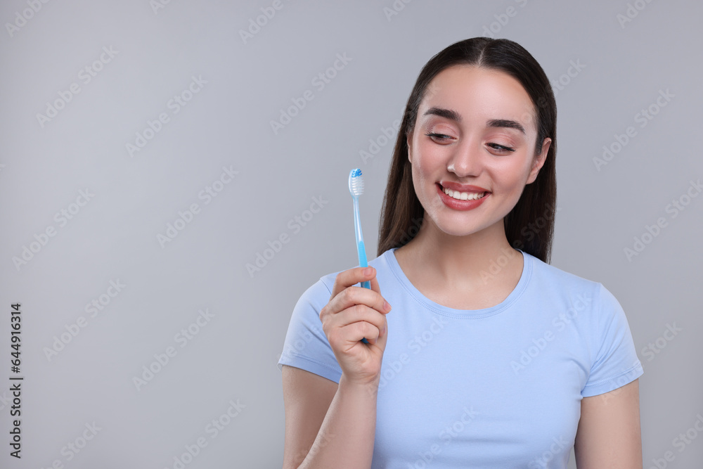 Happy young woman holding plastic toothbrush on light grey background, space for text Happy young woman holding plastic toothbrush on light grey background, space for text
