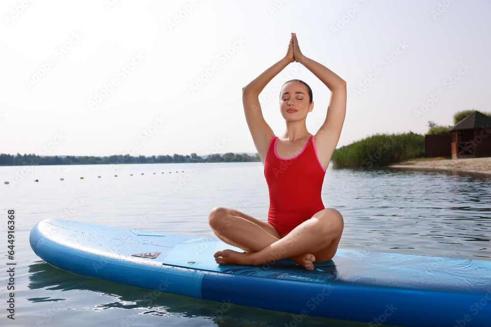 Woman practicing yoga on light blue SUP board on river