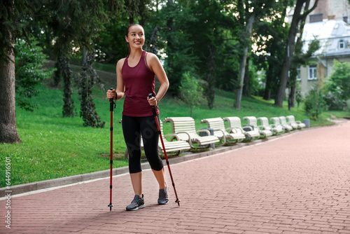 Young woman practicing Nordic walking with poles outdoors. Space for text