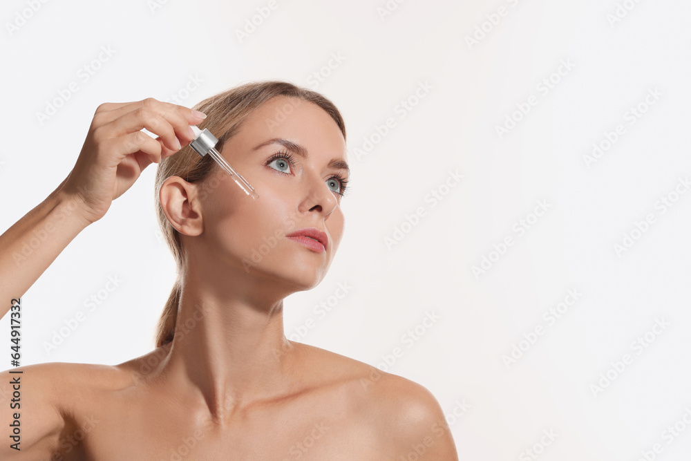 Beautiful woman applying cosmetic serum onto her face on white background, space for text Beautiful woman applying cosmetic serum onto her face on white background, space for text