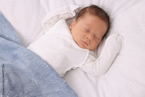 Cute newborn baby sleeping under blue blanket on bed, top view