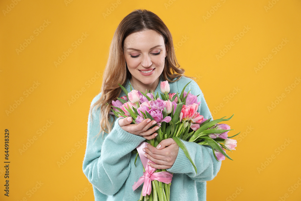 Happy young woman with bouquet of beautiful tulips on yellow background