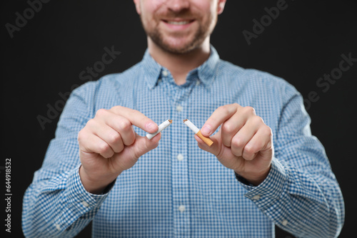 Stop smoking concept. Man holding pieces of broken cigarette on black background, closeup