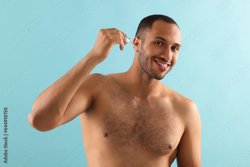 Handsome man applying cosmetic serum onto face on light blue background Handsome man applying cosmetic serum onto face on light blue background