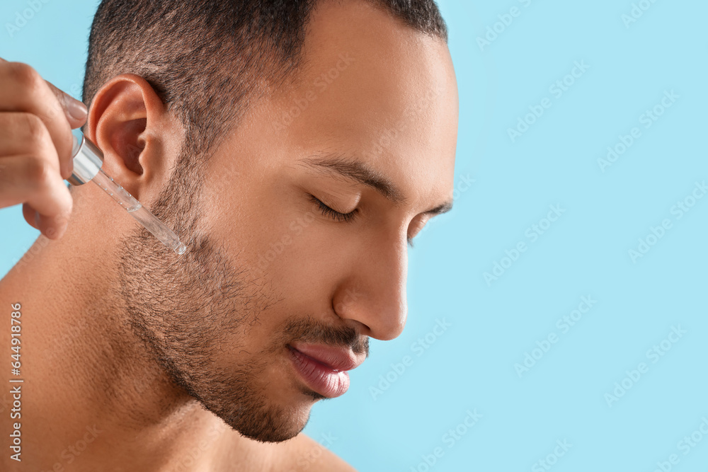 Obraz premium Handsome man applying cosmetic serum onto face on light blue background, closeup. Space for text