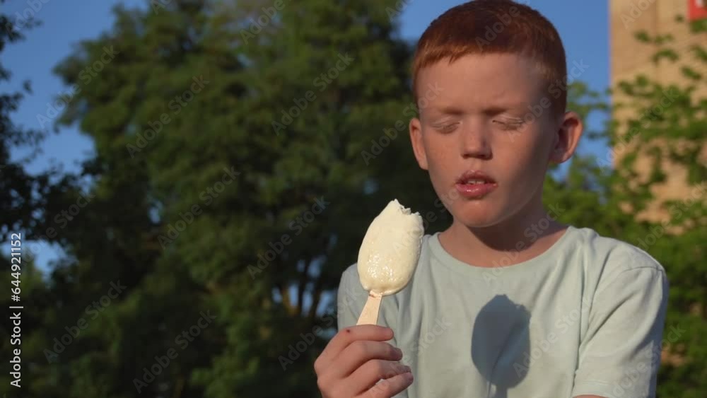 Red-haired boy walks on the street and eats popsicle Red-haired boy walks on the street and eats popsicle