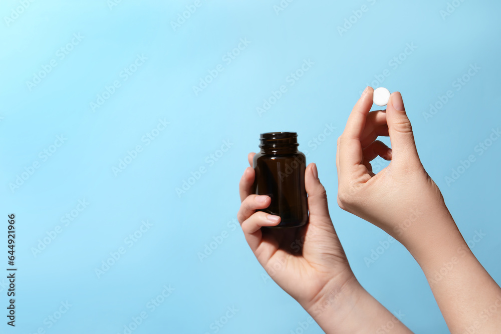 Woman holding pill and bottle on light blue background, closeup. Space for text Woman holding pill and bottle on light blue background, closeup. Space for text