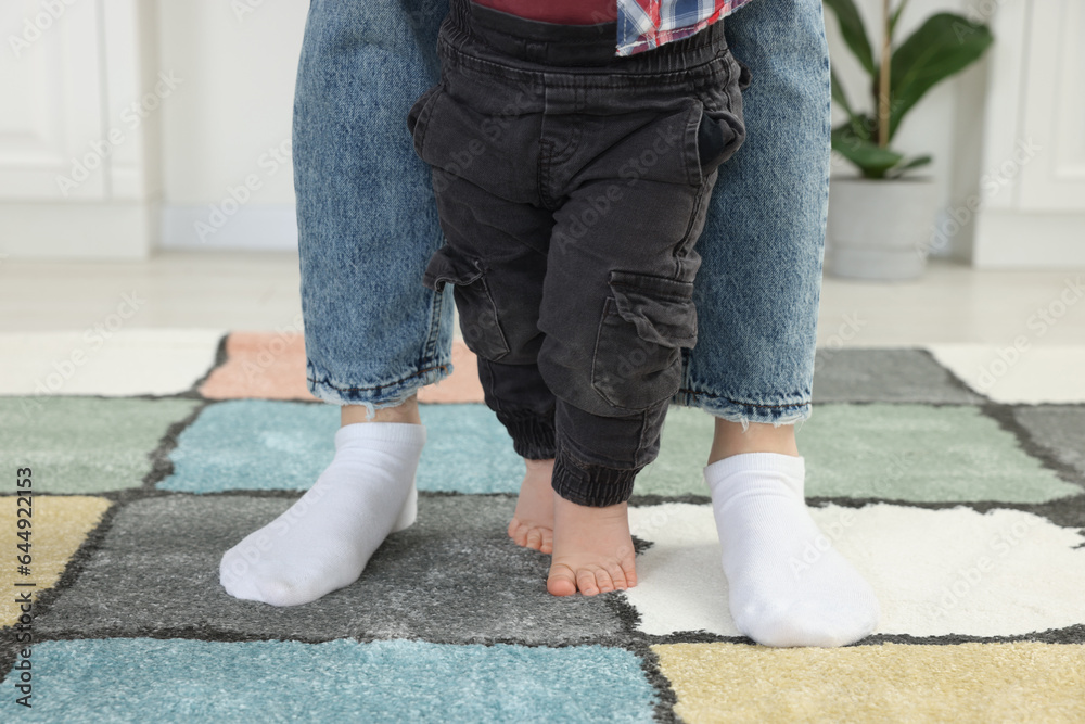 Mother supporting her son while he learning to walk on carpet indoors, closeup Mother supporting her son while he learning to walk on carpet indoors, closeup
