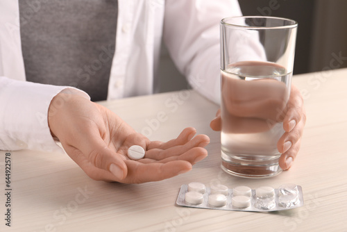 Woman with pills and glass of water at white wooden table, closeup