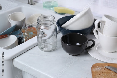 Many dirty utensils and dishware on countertop in messy kitchen