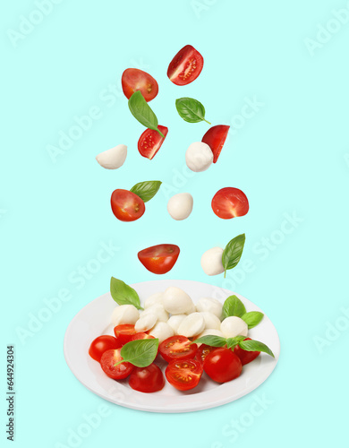 Fresh tomatoes. mozzarella cheese and basil leaves falling onto plate with Caprese salad against light blue background