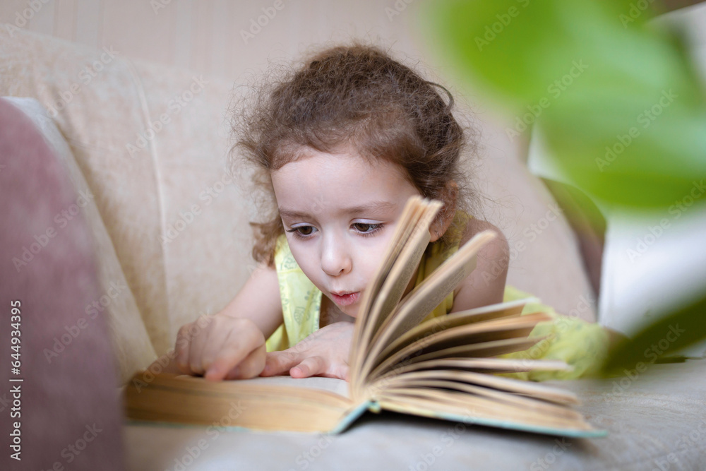 smart little girl reading book at home on couch. child learning read. children's education. smart little girl reading book at home on couch. child learning read. children's education.
