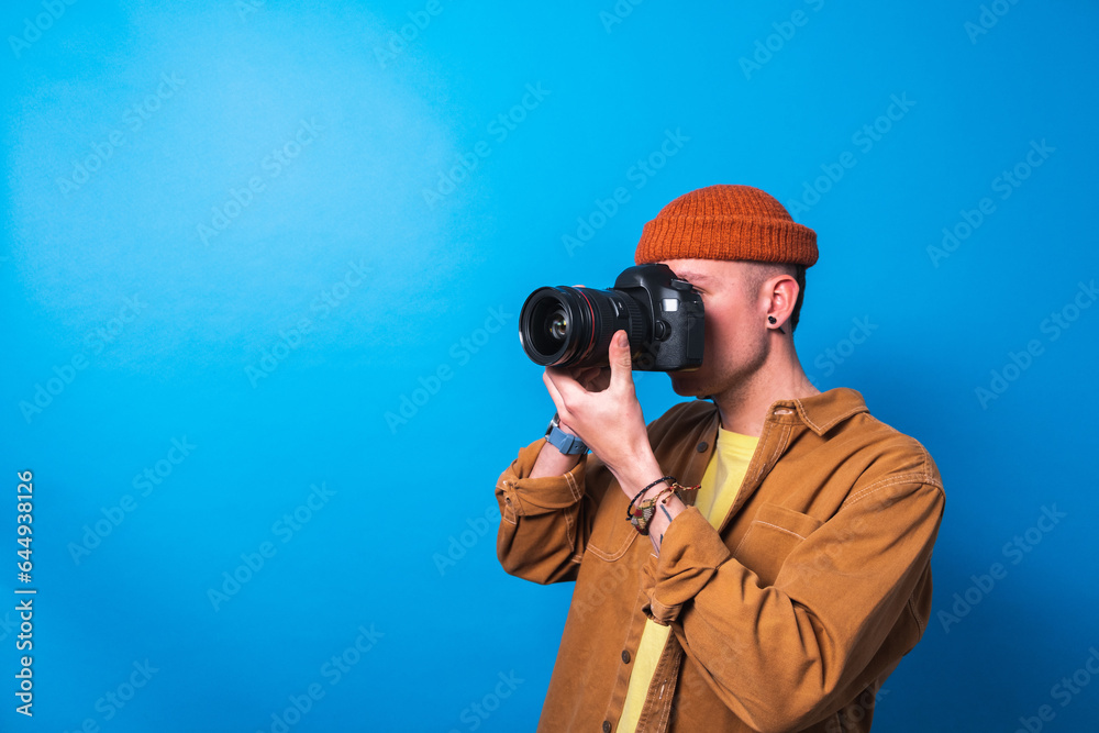 Obraz premium Happy smiling photographer taking pictures checking his camera settings in a studio shooting as content creator in blue background 