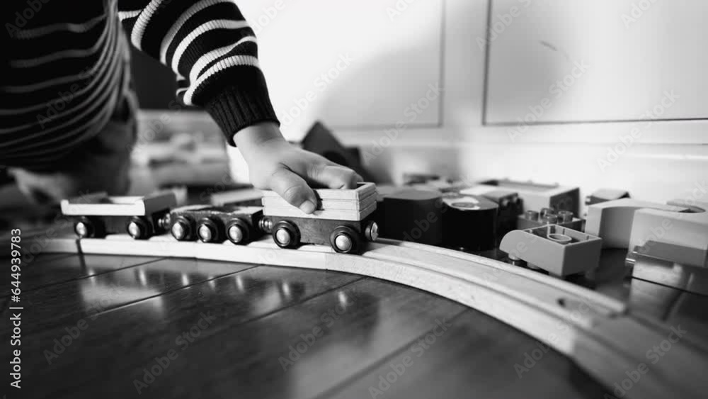 Child hand pushing vintage train wagon on wooden tracks in monochrome, black and white. Little boy playing with retro toy