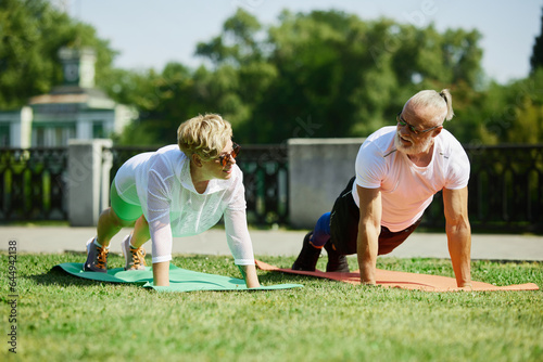 Early morning workout. Mature couple  sportive man and woman training outdoors in park on warm summer day. Standing in plank. Concept of active and sportive lifestyle  age  health care  exercising  ad