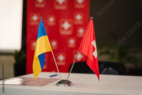Flags of Ukraine and Switzerland. Small flags on table in office of president. Blue and yellow flag. State symbols. Sovereign independent free state. Swiss help, support. Ukraine Recovery Conference. photo