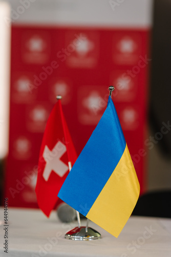 Flags of Ukraine and Switzerland. Small flags on table in office of president. Blue and yellow flag. State symbols. Sovereign independent free state. Swiss help, support. Ukraine Recovery Conference. photo