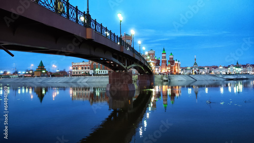 Night view of the high bridge over the river with lights and the embankment in the distance. Evening urban landscape with a bridge