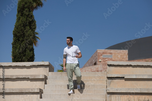 Handsome young man dressed in casual clothes and sunglasses walks down the stairs of a grandstand looking at different parts of the place. © @skuder_photographer
