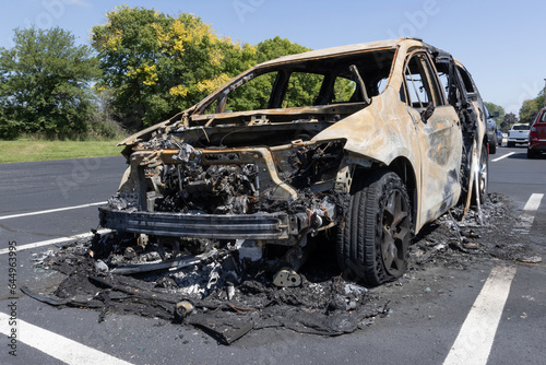 Burned out car in a parking lot. Cautious reminder not to smoke cigarettes and drive.