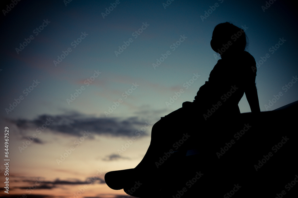 Silhouette of A girl sitting sadly in the back of the car and orange Sunset and blurred golden and blue sky background