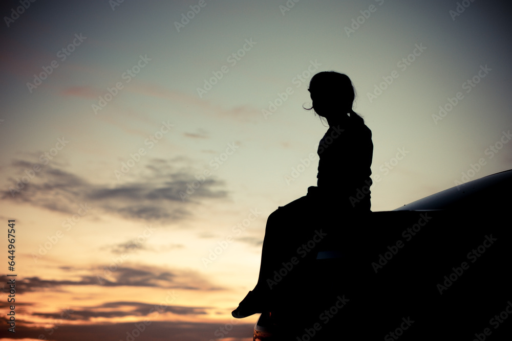 Silhouette of A girl sitting sadly in the back of the car and orange Sunset and blurred goldden and blue sky background