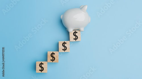 Top view, Flat lay the white piggy bank with USD dollar on wood of cube on blue background with copy space. Financial, Accounting, banking, investment, saving money concept.