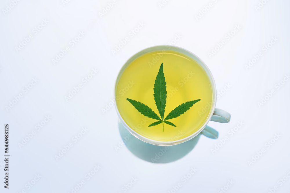 Cannabis tea herbal on white tea cup with cannabis leaf marijuana leaves herb, health tea with hemp leaf plant THC CBD herbs food and medical top view on blue background of table with a reflection Cannabis tea herbal on white tea cup with cannabis leaf marijuana leaves herb, health tea with hemp leaf plant THC CBD herbs food and medical top view on blue background of table with a reflection