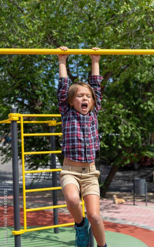 Boy hanging from an exercise bar screaming Boy hanging from an exercise bar screaming