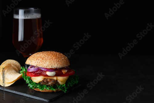 Burger, chips, and a glass of beer in the background on a dark background with space for text.