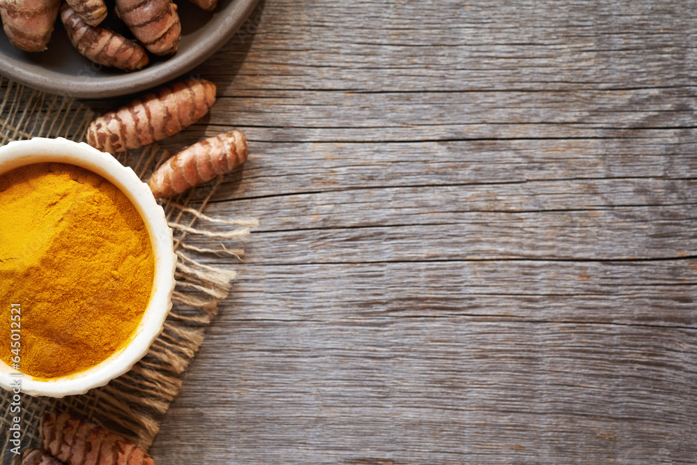 Curcuma powder and fresh root on wooden background with copy space