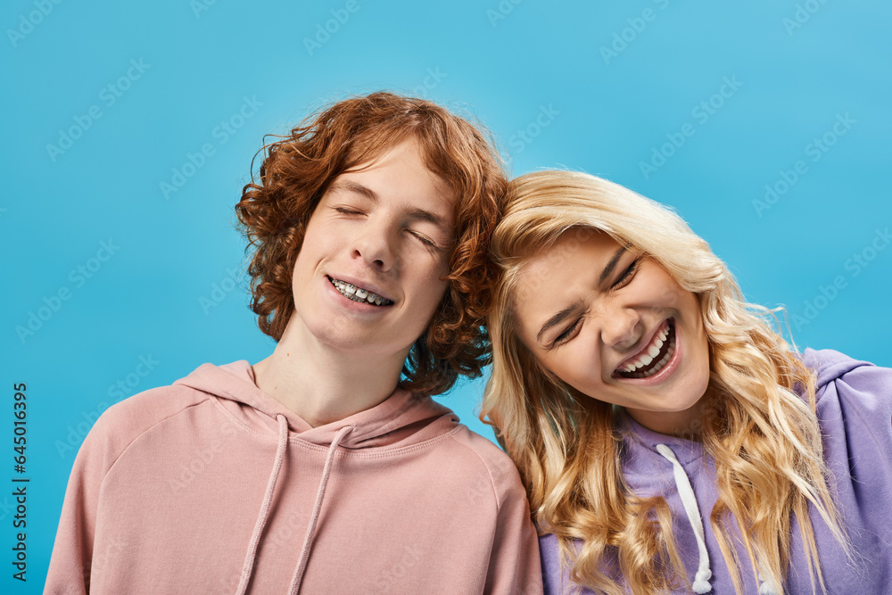 portrait of excited teenage boy and girl in hoodies laughing with closed eyes on blue, happiness portrait of excited teenage boy and girl in hoodies laughing with closed eyes on blue, happiness
