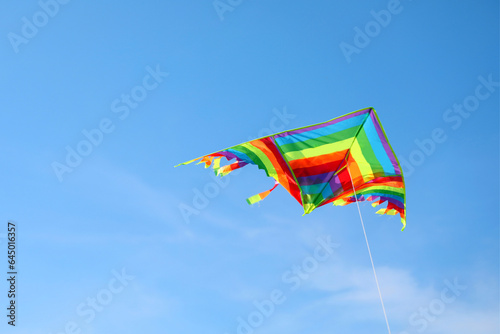 multicolored kite with long colorful tail flying free in blue sky