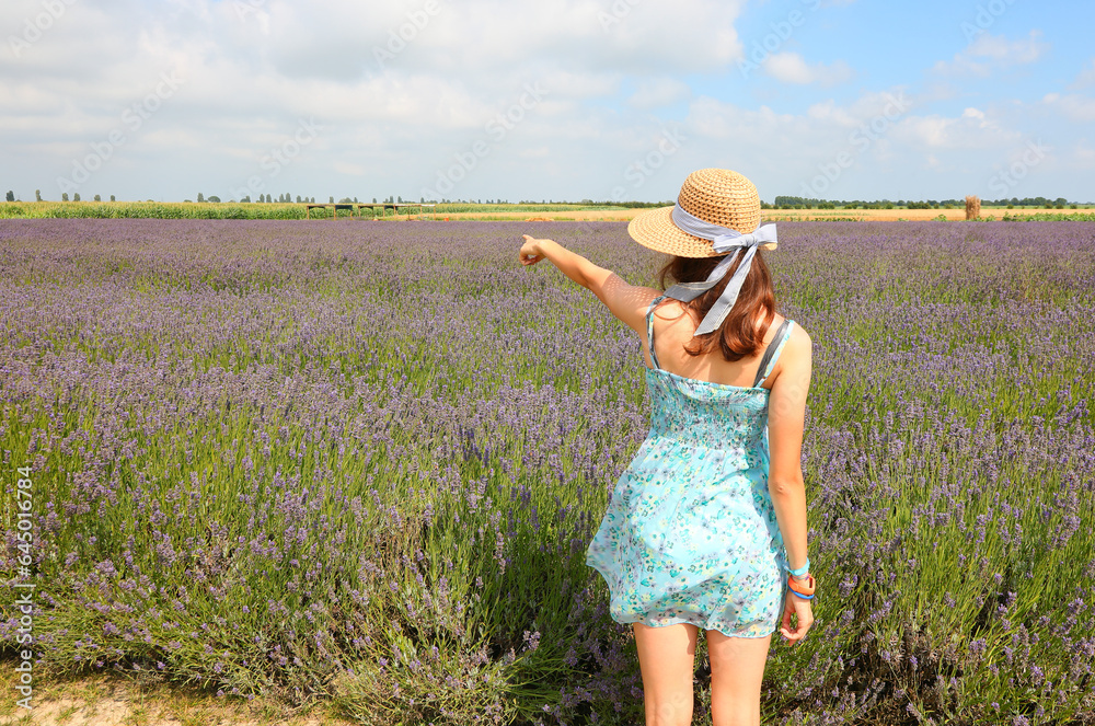 young girl wearing summer dress and straw hat in lavender flower field in the countryside