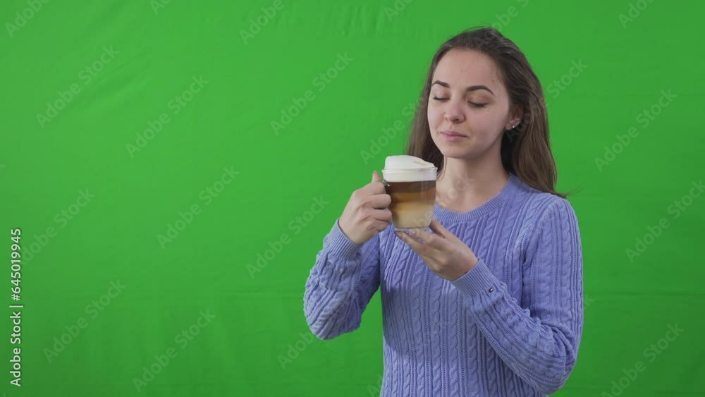 Male hand passing cup of tasty cappuccino with milk foam to young woman standing at chromakey background. Portrait of smiling young Caucasian lady drinking delicious coffee posing at green screen Male hand passing cup of tasty cappuccino with milk foam to young woman standing at chromakey background. Portrait of smiling young Caucasian lady drinking delicious coffee posing at green screen