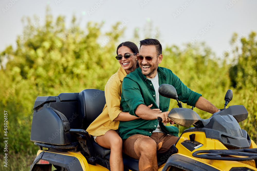 A smiling love couple enjoys the quad bike ride and looks at the nature around them.