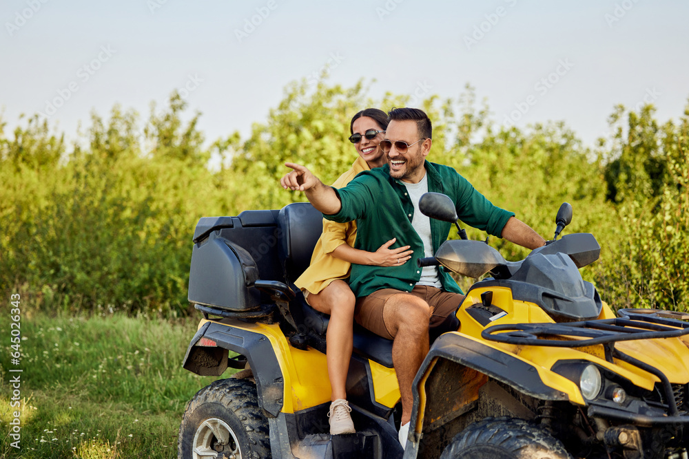 A smiling love couple enjoys the quad bike ride and looks at the nature around them. A smiling love couple enjoys the quad bike ride and looks at the nature around them.