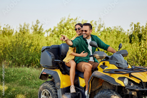 A smiling love couple enjoys the quad bike ride and looks at the nature around them.