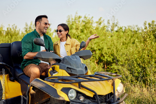 A happy woman stands outdoors beside her boyfriend on a rental quad bike.