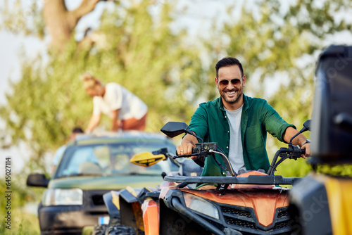 Portrait of a smiling man driving a quad bike in front of the car, off-road.